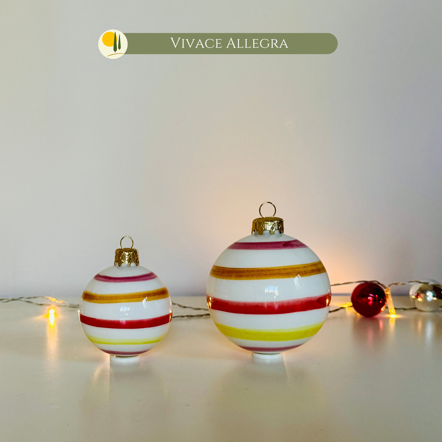 Set di Palline di Natale in Ceramica "Vivace Allegra" di Le Colline, interamente realizzate e dipinte a mano in Italia. L'immagine mostra la palla da 6 cm e quella da 8 cm, caratterizzate da vivaci linee orizzontali colorate (rosso, giallo, verde, blu) su sfondo bianco lucido. Sono ideali per gli addobbi natalizi unici e artigianali, portando sulla tavola e sull'albero l'allegria del design italiano. Perfette idea regalo per gli amanti della decorazione natalizia . Made in Italy