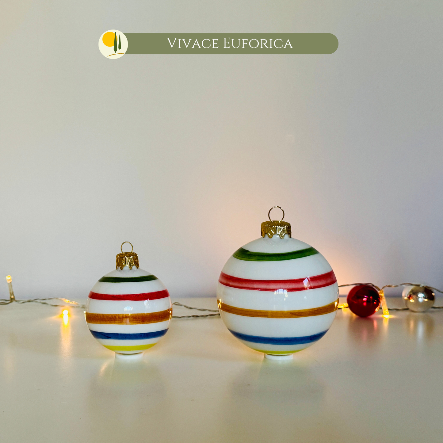 Set of "Vivace Euforica" Ceramic Christmas Ornaments by Le Colline, entirely handcrafted and hand-painted in Italy. The image features the 6 cm and 8 cm baubles, characterized by vibrant, colorful horizontal lines (Red, Yellow, Green, Blue) on a glossy white background. They are ideal for unique and artisanal Christmas tree decorations, bringing the cheer of Italian design to your tree. Perfect as gift idea for lovers of holiday decor or for anyone seeking a unique Made in Italy piece of art.