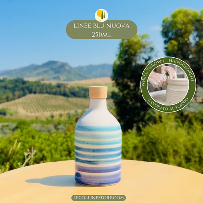 Handcrafted blue striped ceramic bottle with cork stopper, displayed outdoors against vineyards and Mediterranean hills.