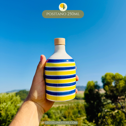 Handcrafted small 250ml blue and yellow striped ceramic bottle with cork stopper, held in hand, inspired by Mediterranean coastal decor.