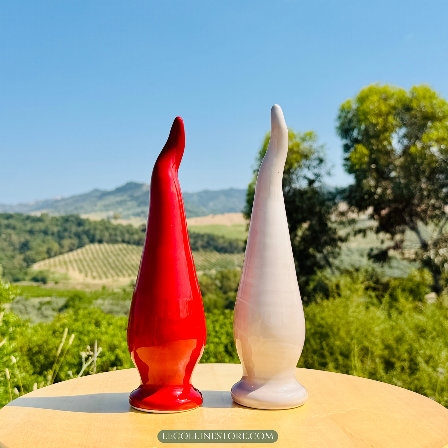 set of one large taupe and one large red ceramic lucky horn with a smooth glossy surface and elongated curved shape. Decorative accent piece for modern home decor, photographed in natural sunlight with a Mediterranean landscape in the background.