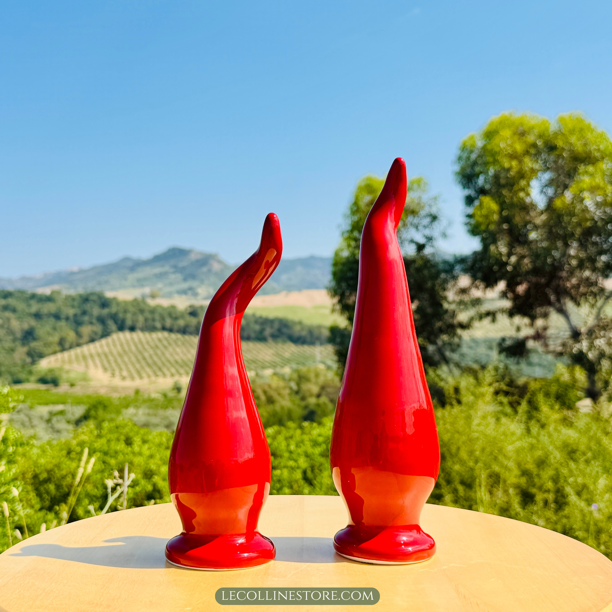 handcrafted ceramic lucky horn with glossy red glaze displayed outdoors against rolling hills and vineyards. Sculptural Italian home decor piece with an elegant curved silhouette and reflective finish.