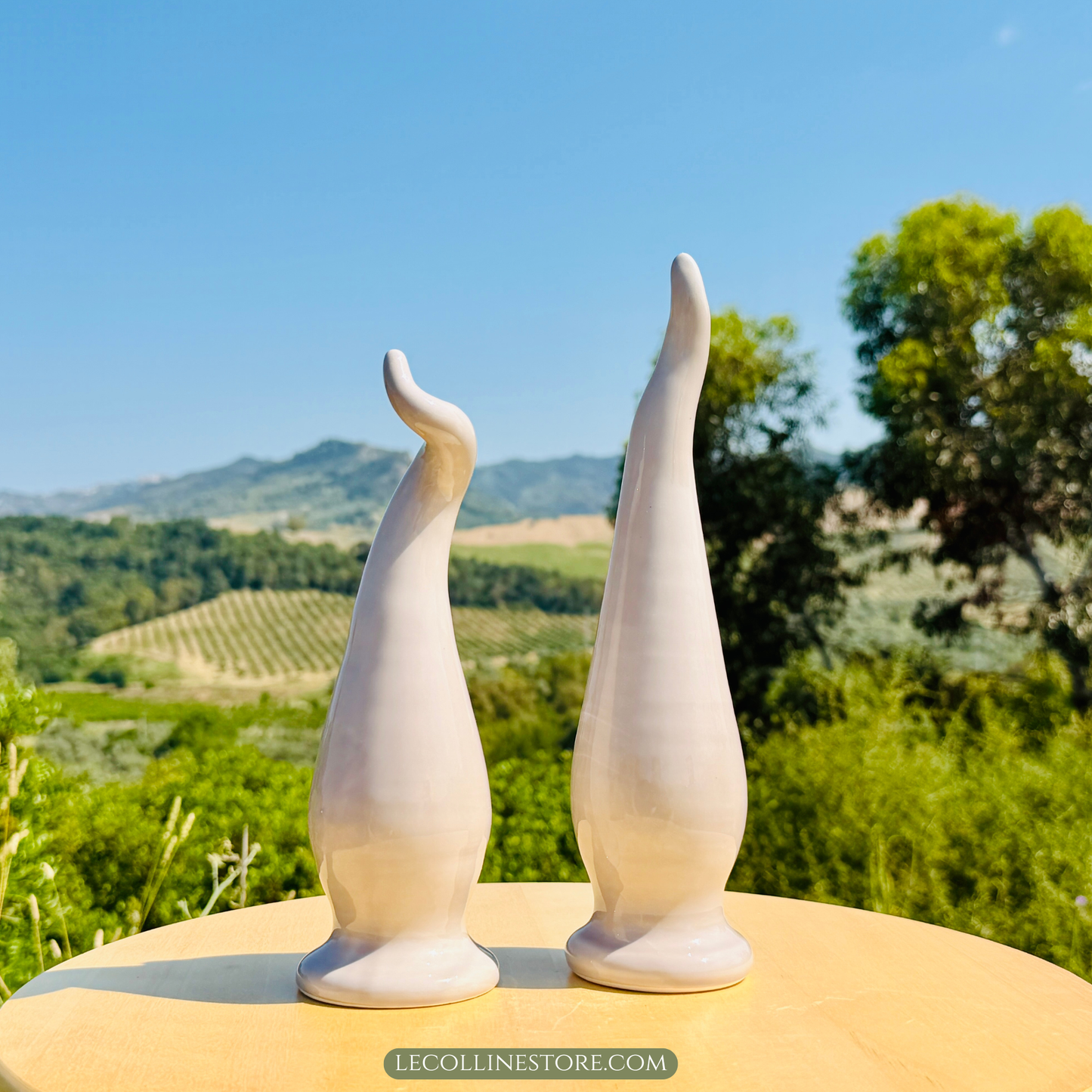 set of two taupe ceramic lucky horn with a smooth glossy surface and elongated curved shape. Decorative accent piece for modern home decor, photographed in natural sunlight with a Mediterranean landscape in the background.