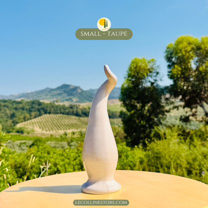 Small taupe ceramic lucky horn with a smooth glossy finish and minimalist sculptural shape. Elegant decorative object for modern home decor, displayed in natural Mediterranean surroundings.