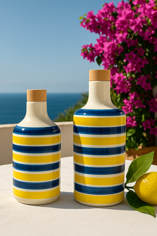 Zwei handgefertigte Keramikflaschen mit gelb-blauen Streifen und Holzdeckeln, ideal als Olivenölspender oder Essigflaschen. Mediterranes Design, inspiriert von der Amalfiküste, perfekt für Küche, Esstisch oder als dekoratives Element im Freien. Auf einem Tisch mit Zitronenblatt vor dem Meer und blühender Bougainvillea platziert – ein Hauch Italien für jedes Zuhause.